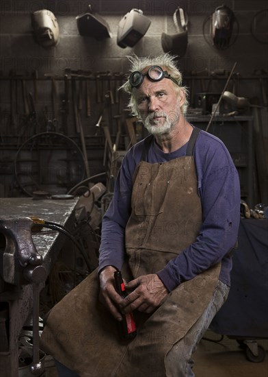 Portrait of serious Caucasian blacksmith in workshop drinking beer