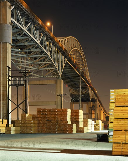 Piles of lumber under bridge at night