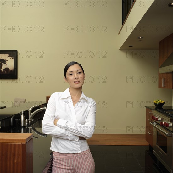 Asian woman leaning on counter in kitchen