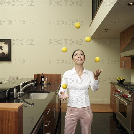 Asian woman juggling lemons in kitchen