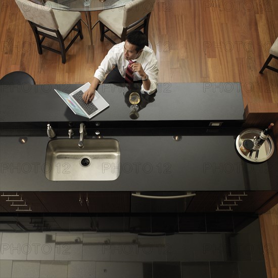 Asian man typing on laptop in kitchen