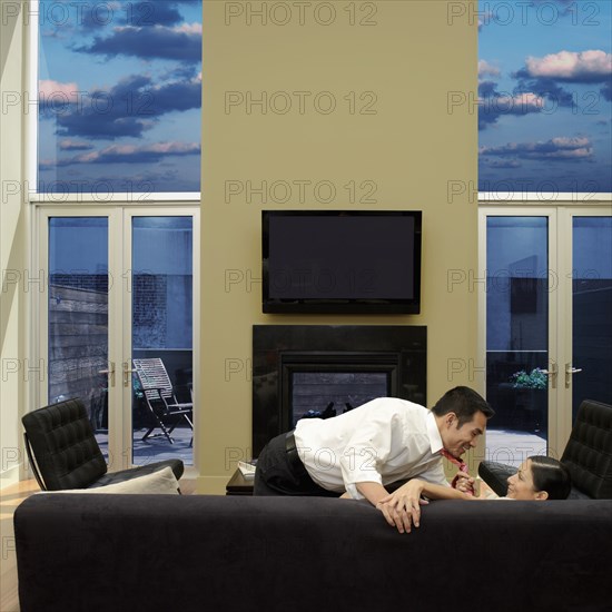 Asian woman pulling husband down onto sofa