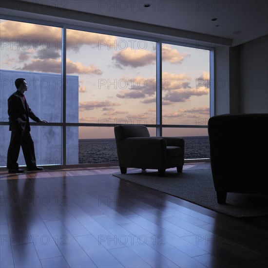 Asian man looking out window at dusk