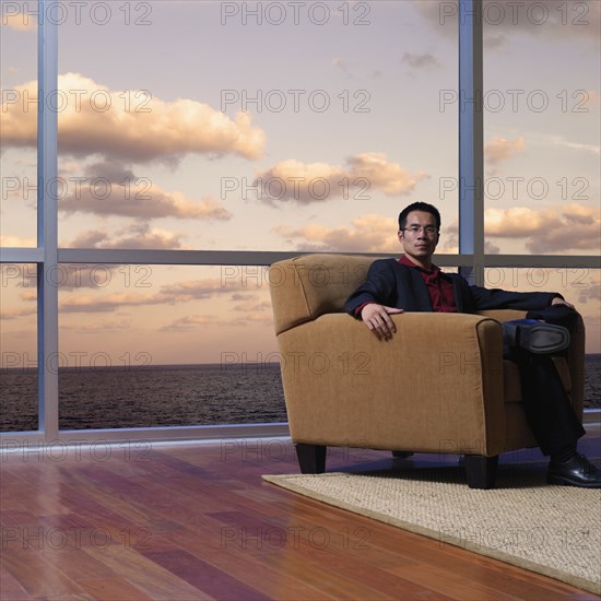 Asian man sitting next to window overlooking water