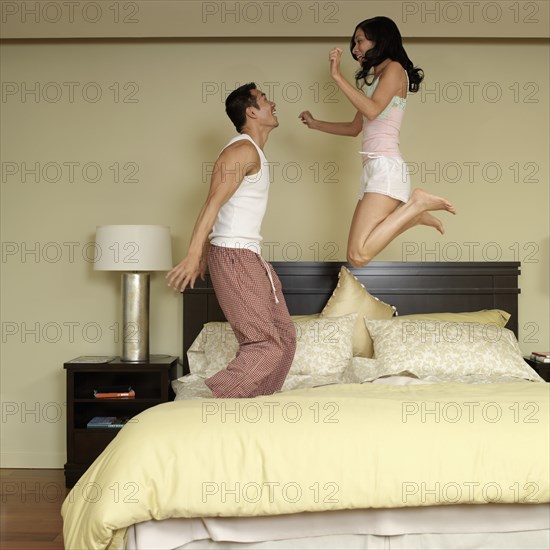 Asian couple jumping on bed