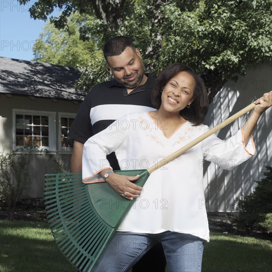 Husband watching woman playing air guitar with rake