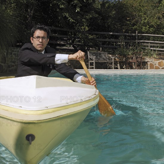 Mixed race businessman rowing boat in swimming pool