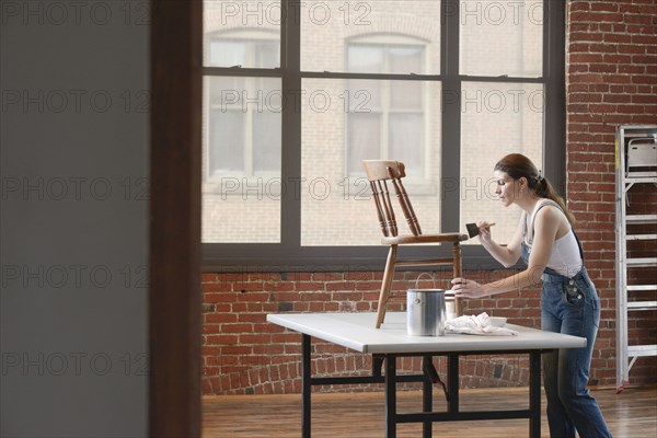 Mixed race woman painting chair in loft