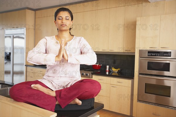 Indian woman meditating in kitchen