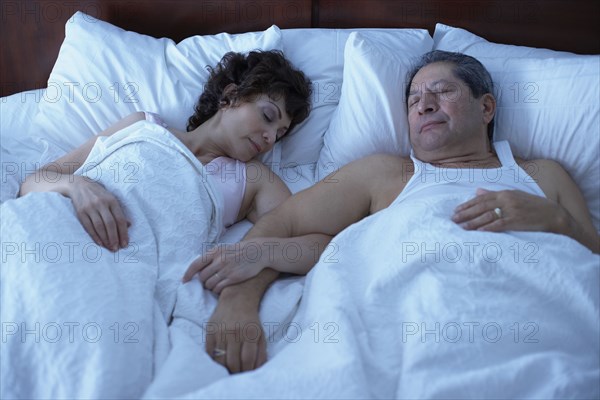 Multi-ethnic couple sleeping in bed arm in arm