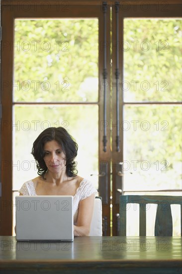 Confident Middle Eastern woman typing on laptop in dining room