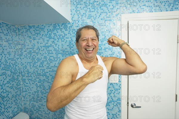 Hispanic man flexing his biceps in bathroom