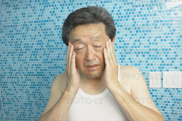 Asian man rubbing his temples in bathroom