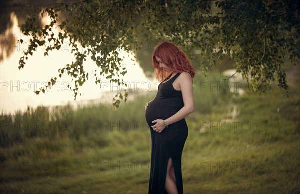 Caucasian expectant mother holding belly under tree branches