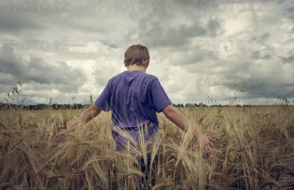 Caucasian boy walking in field of wheat