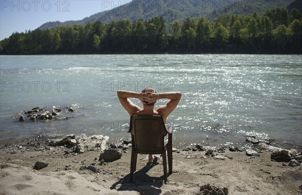 Caucasian man sitting in chair sunbathing near river