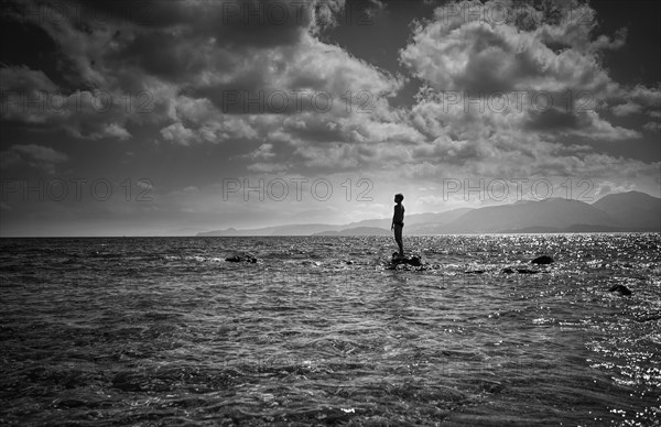 Silhouette of Caucasian boy standing on rock in ocean