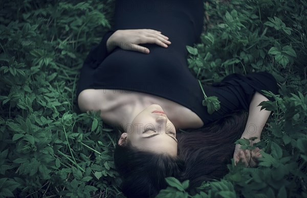 Caucasian woman wearing dress laying in green foliage