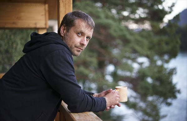 Caucasian man leaning on railing drinking coffee