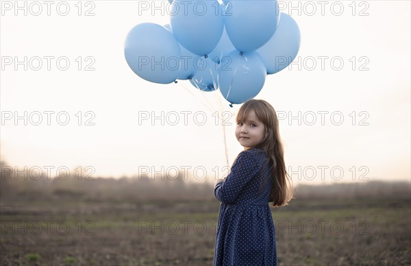 Caucasian girl holding blue helium balloons