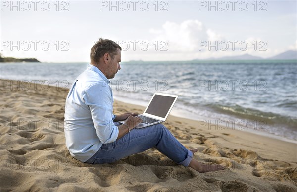 Caucasian man sitting on beach using laptop