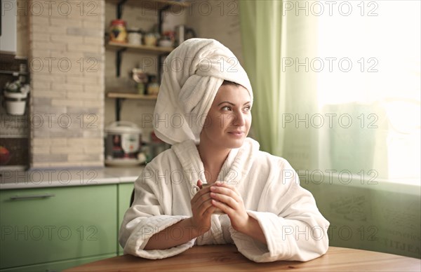 Caucasian woman in bathrobe and towel warming hands on cup