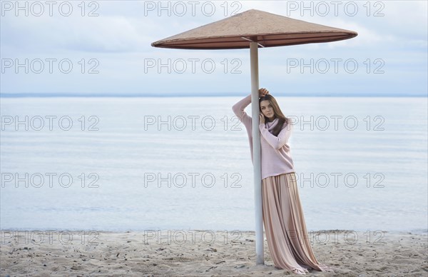Pensive Caucasian woman leaning on beach umbrella