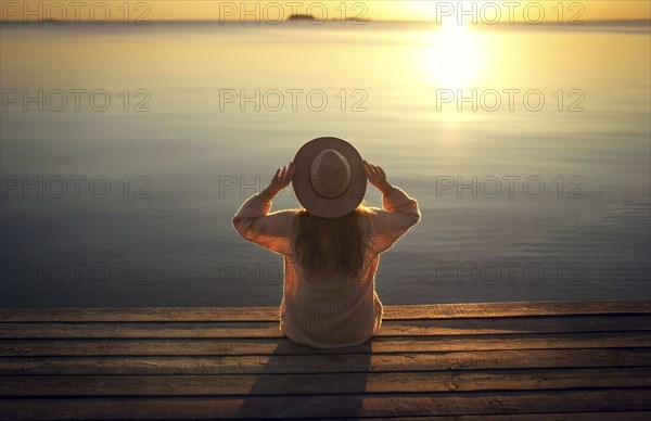 Caucasian woman sitting on dock of lake admiring sunset