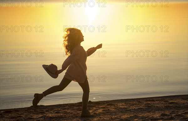 Caucasian woman running on beach holding hat