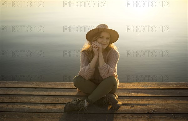 Smiling Caucasian woman sitting on dock of lake
