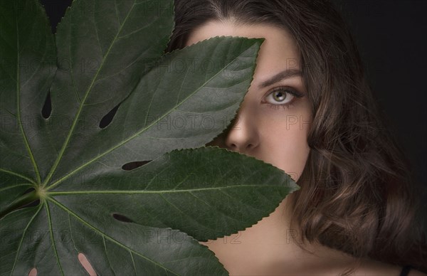 Caucasian woman hiding behind green leaf