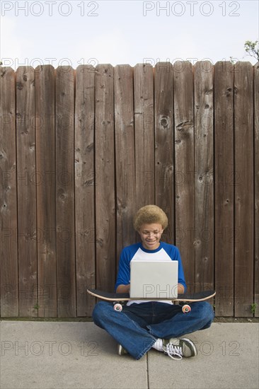 Mixed race boy typing on laptop outdoors