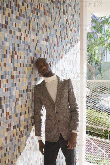 African man in tweed jacket leaning against tiled wall