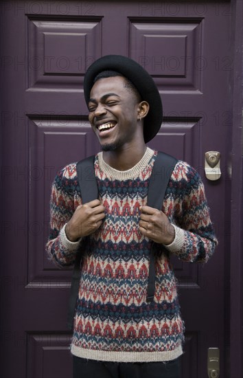 Laughing Black man wearing backpack near purple door