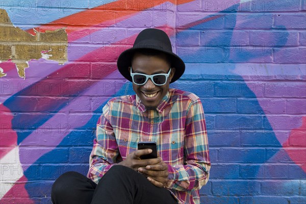 Black man using cell phone near colorful wall