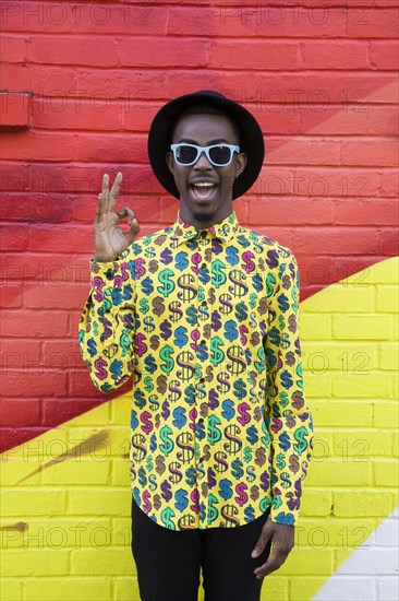 Black man in sunglasses making okay sign near colorful wall