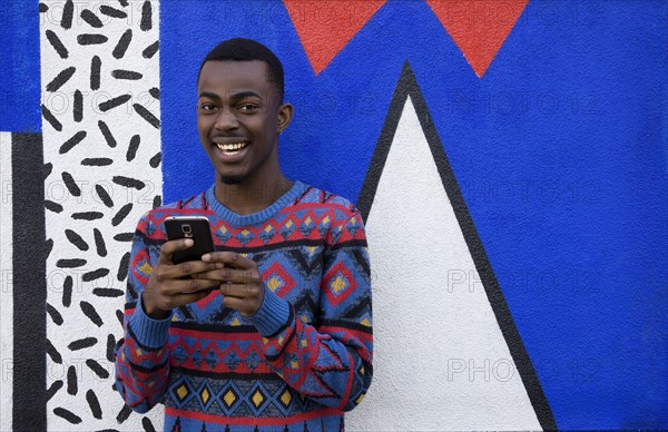 Black man using cell phone near colorful wall