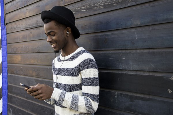 Black man listening to mp3 player near wooden wall