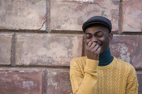 Black man laughing near brick wall