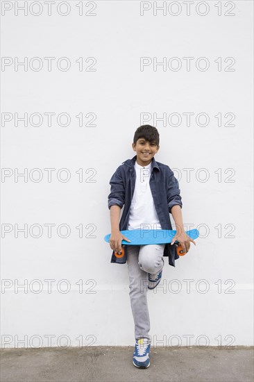 Asian boy holding skateboard at wall