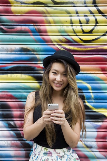 Asian woman using cell phone near graffiti wall