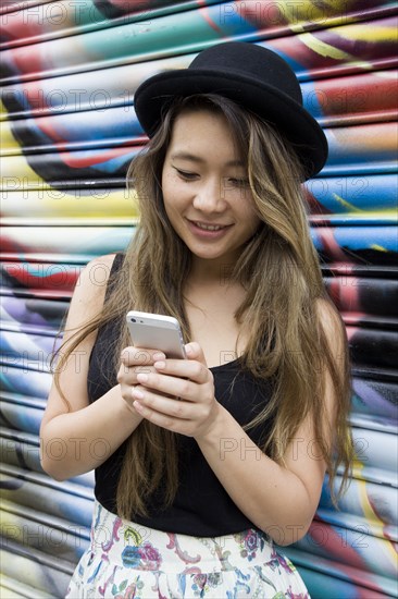 Asian woman using cell phone near graffiti wall