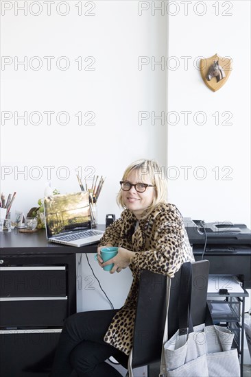 Caucasian woman drinking coffee at desk with laptop