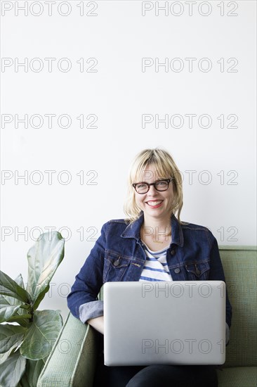 Caucasian woman sitting on sofa using laptop