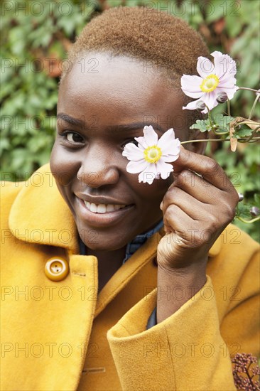 Portrait of smiling Black woman covering eye with flower