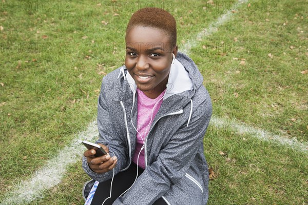 Black woman sitting on field listening to cell phone