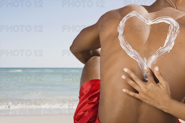 Hispanic woman drawing heart in sunscreen on boyfriend's back