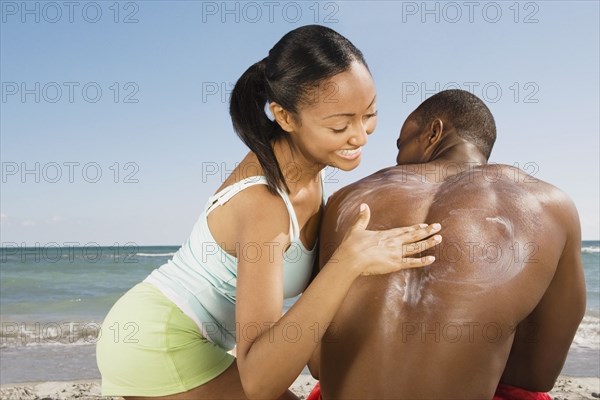 Hispanic woman rubbing sunscreen on boyfriend's back