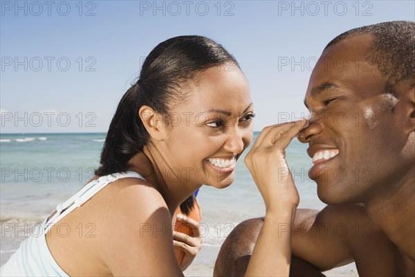 Hispanic woman rubbing sunscreen on boyfriend's nose