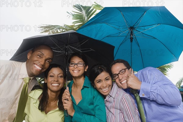 Hispanic businesspeople standing under umbrellas